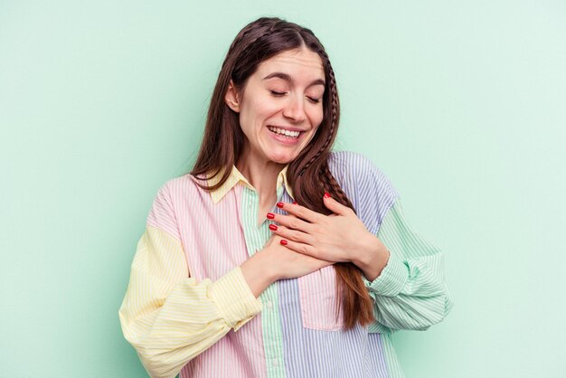 La giovane donna caucasica isolata su sfondo verde ha un'espressione amichevole che preme il palmo sul petto Concetto di amore