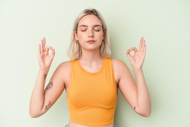 La giovane donna caucasica isolata su sfondo verde si rilassa dopo una dura giornata di lavoro, sta eseguendo yoga.