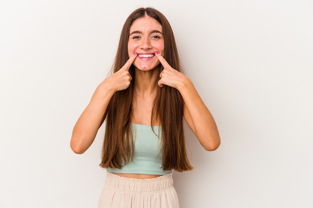 La giovane donna caucasica isolata sui sorrisi bianchi del fondo, indicando le dita alla bocca.