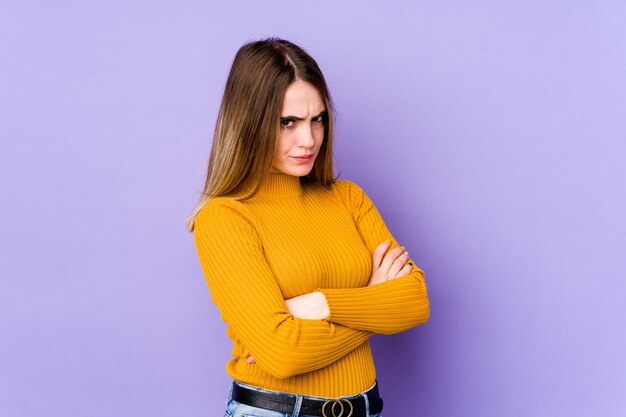 La giovane donna caucasica isolata sul fronte accigliato muro viola per il dispiacere, tiene le braccia conserte