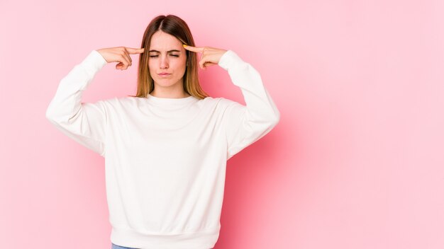 La giovane donna caucasica isolata sul rosa si è concentrata su un compito, mantenendo l'indice che indica la testa.