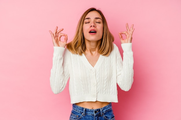 La giovane donna caucasica isolata sul rosa si rilassa dopo una dura giornata di lavoro, sta eseguendo lo yoga.