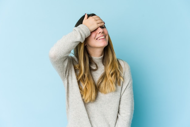 La giovane donna caucasica isolata sulla parete blu ride con gioia tenendo le mani sulla testa. Concetto di felicità.