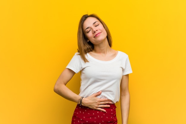 La giovane donna caucasica naturale tocca la pancia, sorride delicatamente, mangiando e concetto di soddisfazione.