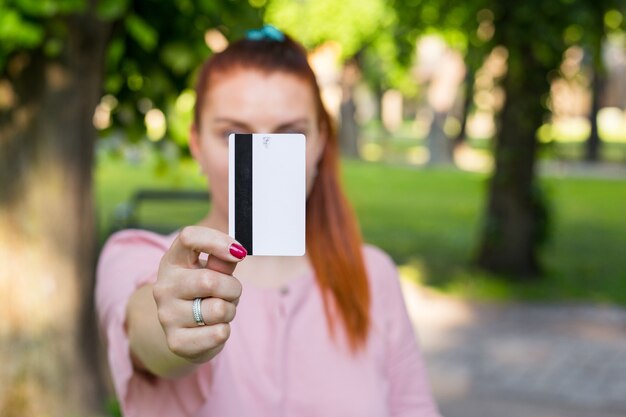 La giovane donna caucasica resta nel parco e mostra la carta di credito bianca con la linea nera del magnete.