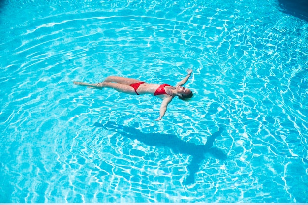La giovane donna caucasica si rilassa e si gode le vacanze estive galleggianti sull'acqua in piscina nella residenza dell'hotel
