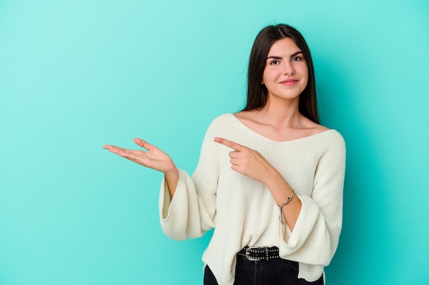 La giovane donna caucasica sull'azzurro ha eccitato che tiene uno spazio della copia sul palmo.