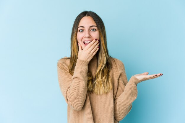 La giovane donna caucasica sull'azzurro tiene lo spazio della copia su una palma, tiene la mano sulla guancia. Stupito e deliziato.