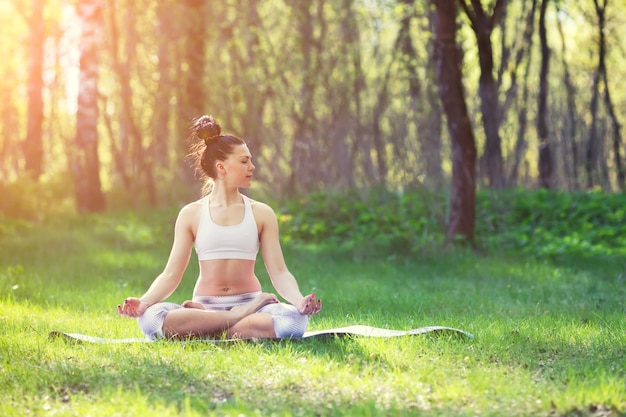 La giovane donna che fa gli esercizi di yoga nel concetto di stile di vita di salute del parco della città di estate