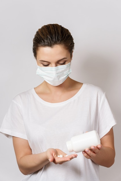 La giovane donna che indossa la maschera per il viso tiene in mano una pillola bianca