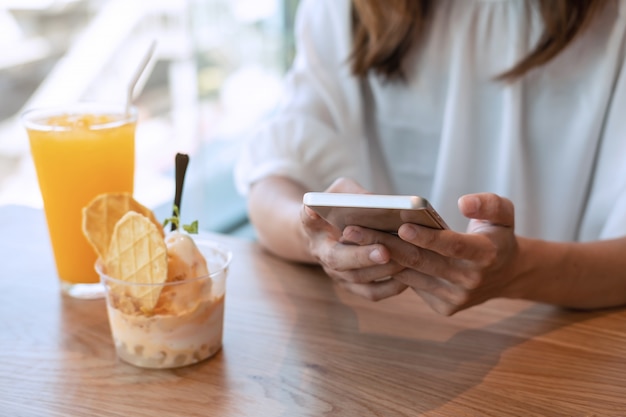 La giovane donna che per mezzo dello Smart Phone e gode del cibo del dessert in caffè