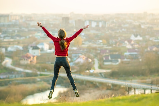 La giovane donna che salta con le braccia tese e le gambe all'aperto su una città lontana. Concetto di relax, libertà e benessere.