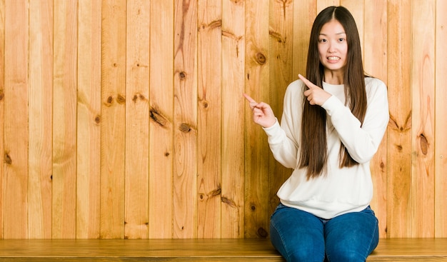 La giovane donna che si siede su un posto di legno ha colpito l'indicare con i dito indice uno spazio della copia