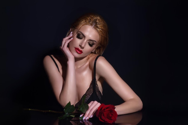 La giovane donna che tiene la ragazza di bellezza rosa con la rosa rossa vicino allo studio del fronte ha sparato i fiori romantici della donna sexy