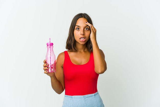 La giovane donna che tiene un milkshake isolato sul muro bianco grida forte, tiene gli occhi aperti e le mani tese