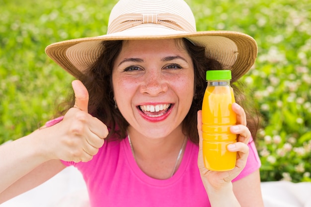 La giovane donna che tiene una bottiglia con succo e che mostra i pollici aumenta il gesto.