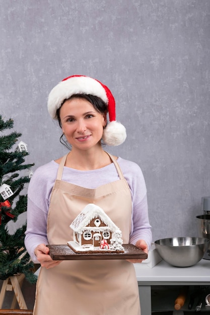 La giovane donna chef nel cappello di Capodanno tiene in mano la casa di marzapane Telaio verticale