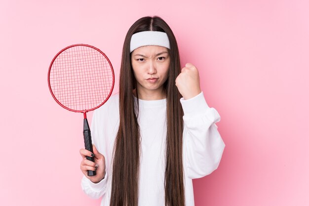 La giovane donna cinese che gioca badminton ha isolato mostrando il pugno, espressione facciale aggressiva.