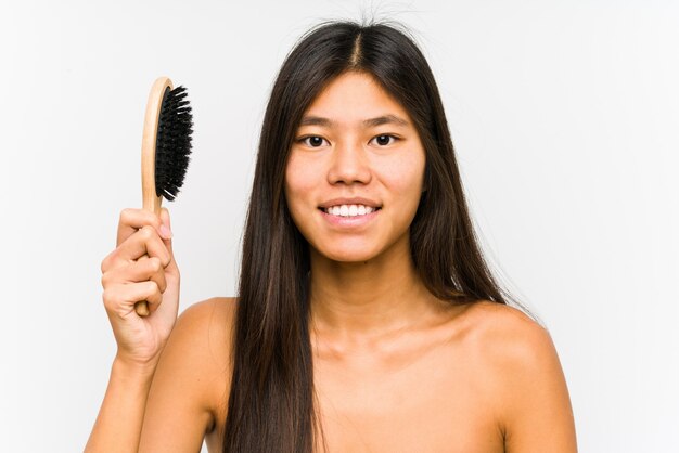 La giovane donna cinese che giudica una spazzola per i capelli ha isolato felice, sorridente e allegro.