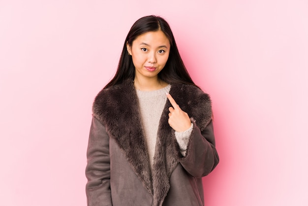 La giovane donna cinese che indossa un cappotto ha isolato indicare con il dito come se l'invito si avvicini.
