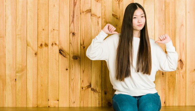 La giovane donna cinese che si siede su un posto di legno si sente orgogliosa e sicura di sé, esempio da seguire.