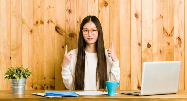 La giovane donna cinese che studia sulla sua scrivania punta verso il basso con le dita, sensazione positiva.