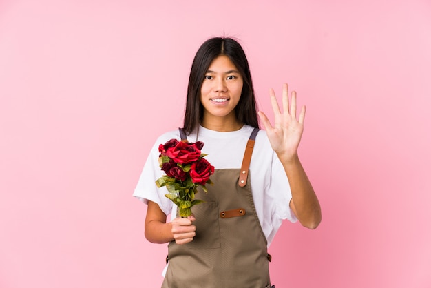 La giovane donna cinese del giardiniere che tiene un numero di mostra allegro sorridente isolato rose cinque con le dita.