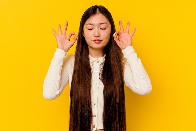 La giovane donna cinese isolata sul giallo si rilassa dopo una dura giornata di lavoro, sta eseguendo lo yoga.