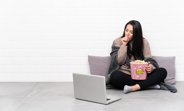 La giovane donna colombiana che tiene in mano una ciotola di popcorn e mostra un film su un laptop soffre di tosse e si sente male