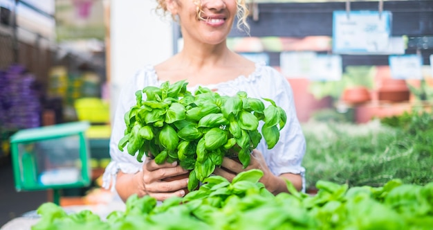 La giovane donna con capelli ricci biondi sceglie una piantina di basilico in un negozio. Concetto di cura e passione per la natura