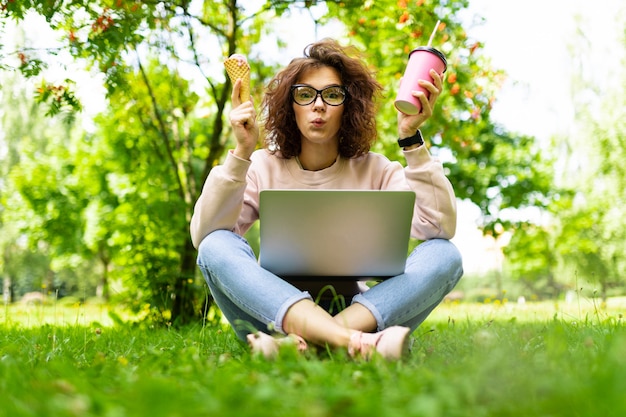 La giovane donna con gli occhi verdi si siede su un'erba con un computer portatile