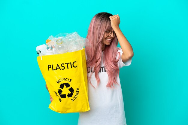 La giovane donna con i capelli rosa che tiene in mano una borsa piena di bottiglie di plastica da riciclare isolata su sfondo blu ha realizzato qualcosa e intendeva la soluzione