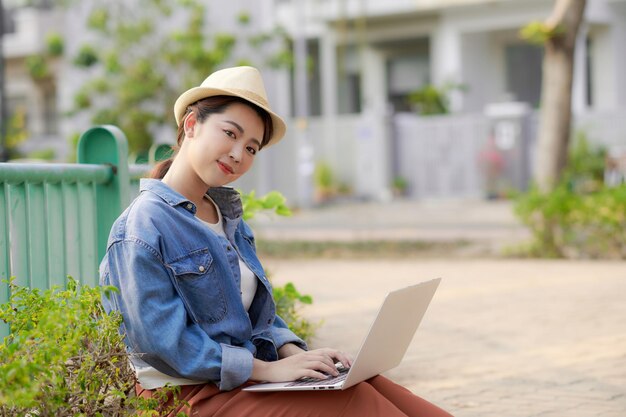 La giovane donna con il computer portatile si siede sul divano nel parco in una giornata di sole