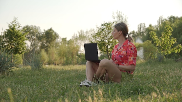 La giovane donna con il computer portatile si siede sull'erba nel parco