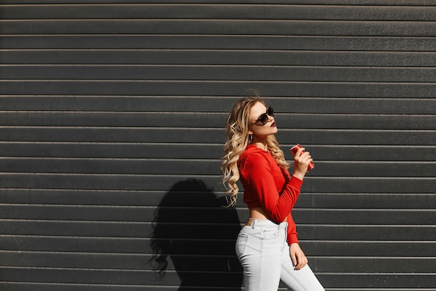 La giovane donna con l'ente perfetto che indossa una maglia con cappuccio rossa e gli occhiali da sole sta posando all'aperto.