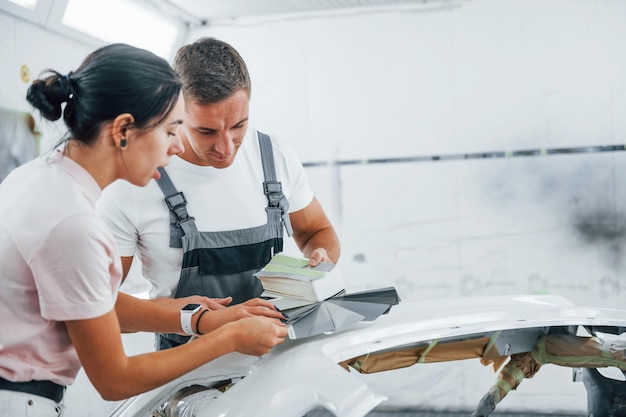 La giovane donna con l'uomo lavora insieme nel garage di riparazione dell'automobile