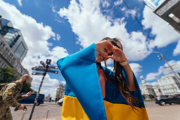 La giovane donna con la bandiera ucraina mostra il cuore con le mani