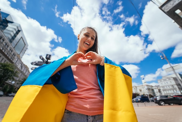 La giovane donna con la bandiera ucraina mostra il cuore con le mani