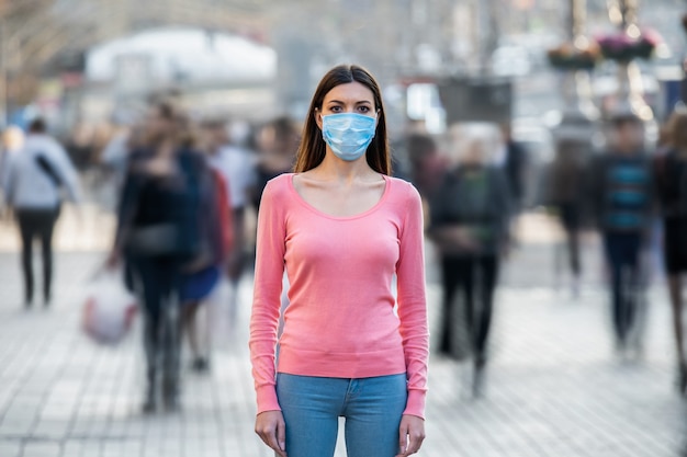 La giovane donna con la maschera medica sul viso si trova sulla strada affollata