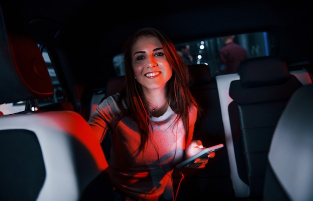 La giovane donna con lo smartphone è all'interno della nuovissima automobile moderna.