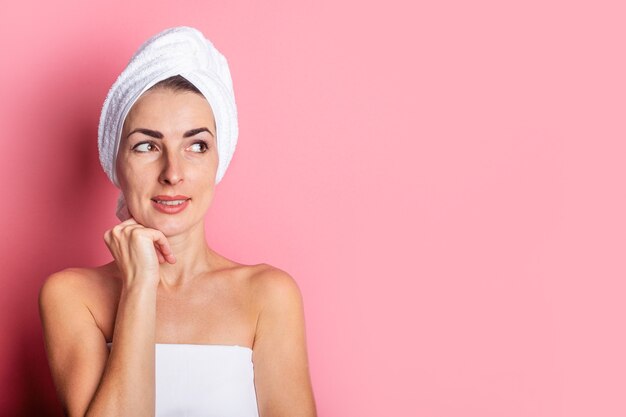 La giovane donna con un asciugamano in testa guarda di lato su uno sfondo rosa.