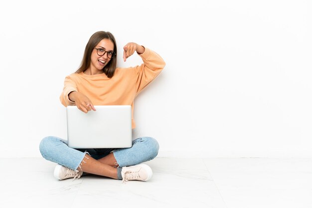 La giovane donna con un laptop seduta sul pavimento ti punta il dito contro mentre sorride