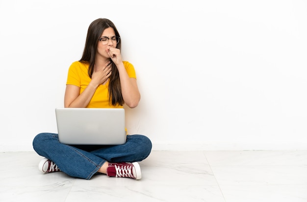 La giovane donna con un laptop seduto sul pavimento soffre di tosse e si sente male