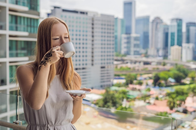 La giovane donna con una foto sulla mano di henné mehendi beve il caffè al mattino sul balcone