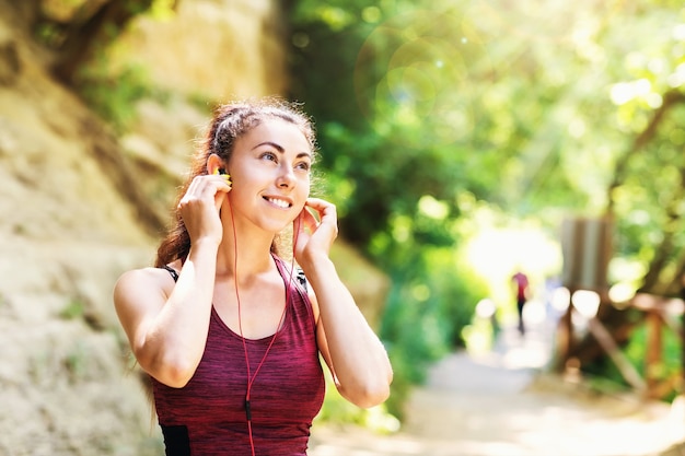 La giovane donna contenta in abbigliamento sportivo nel parco ascolta la musica sulle cuffie mentre si esercita sulla strada