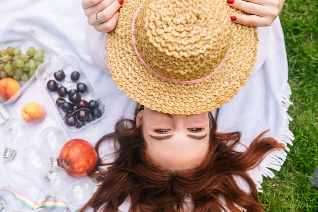 La giovane donna copre il viso con un cappello mentre è sdraiata sul prato