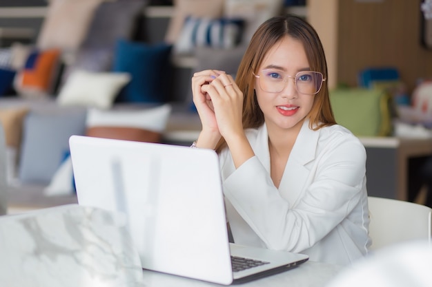 La giovane donna d'affari asiatica professionale con gli occhiali lavora nello spazio di co-working con il lavoro di carta del computer portatile (concetto di donna d'affari).