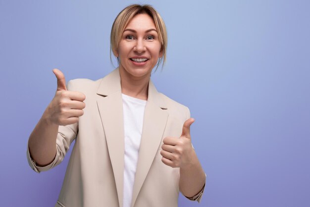 La giovane donna d'affari bionda positiva in giacca mostra classe come sullo sfondo dello studio