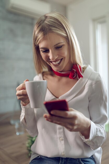 La giovane donna d'affari di felicità ha una pausa caffè e usa lo smartphone in ufficio.