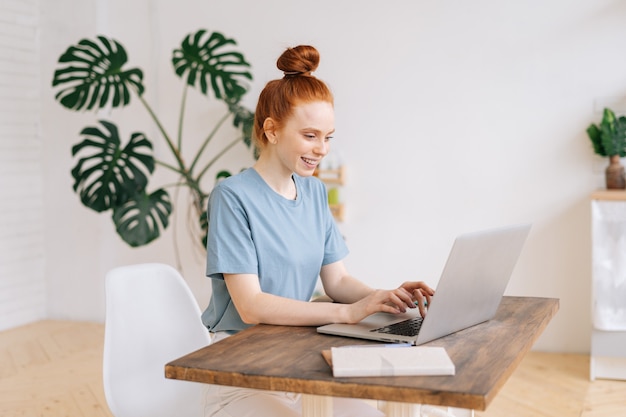 La giovane donna d'affari sorridente allegra dei capelli rossi sta lavorando al computer portatile alla scrivania